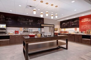 A breakfast area with a counter, a sign that says 'HAPPY BREAKFAST STARTS HERE', and various food items displayed. - Hampton Inn Chicago Orland Park (Orland Park)