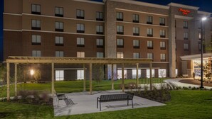Un hotel Hampton Inn con una zona de estar cubierta al aire libre, un césped bien cuidado y fachada de ladrillo.