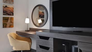Una habitación moderna con televisión, escritorio con lámpara, una silla y una obra de arte en la pared.