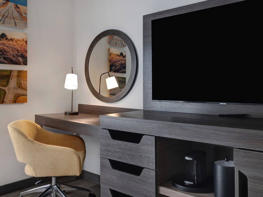 Una habitación moderna con televisión, escritorio con lámpara, una silla y una obra de arte en la pared.