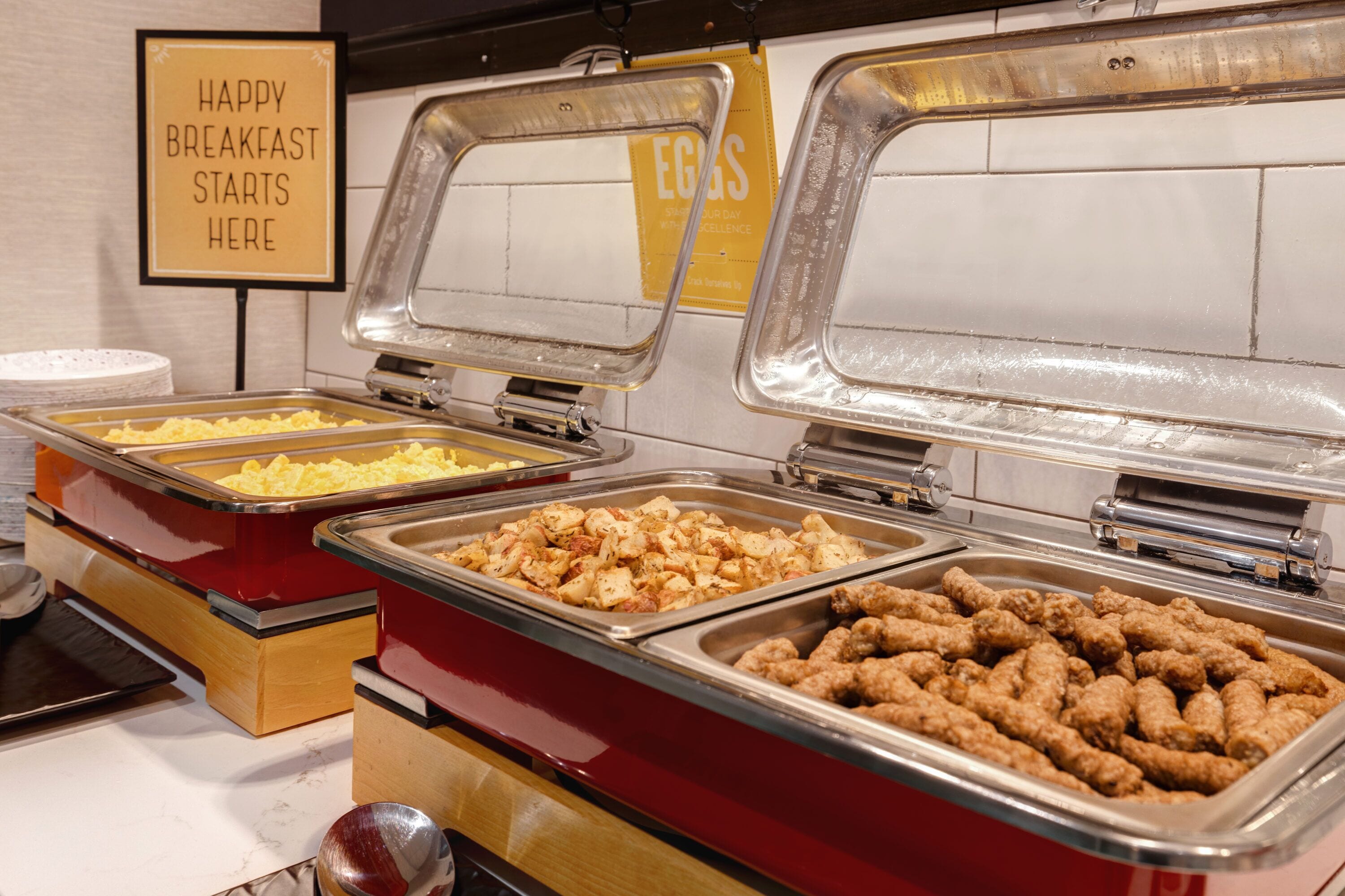 A buffet with various food options including scrambled eggs, potatoes, and chicken nuggets.