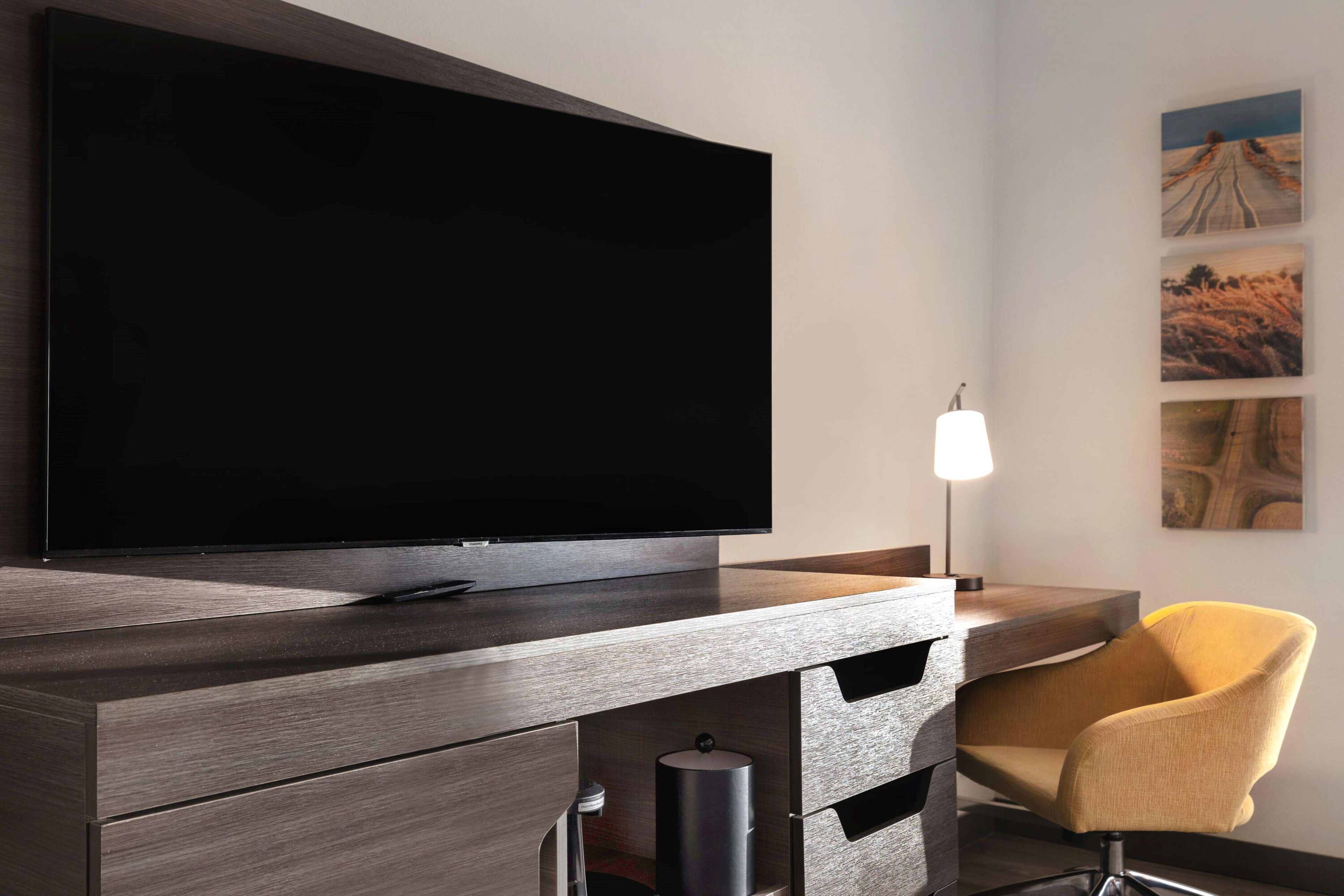 A modern room with a flat-screen TV mounted on a wooden cabinet, a yellow armchair, and a wall with framed artwork.