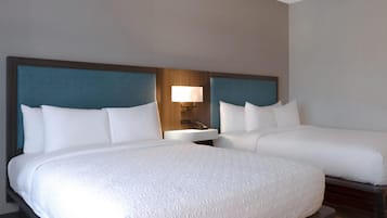 A hotel room with two beds, a nightstand, a lamp, and a wooden headboard.