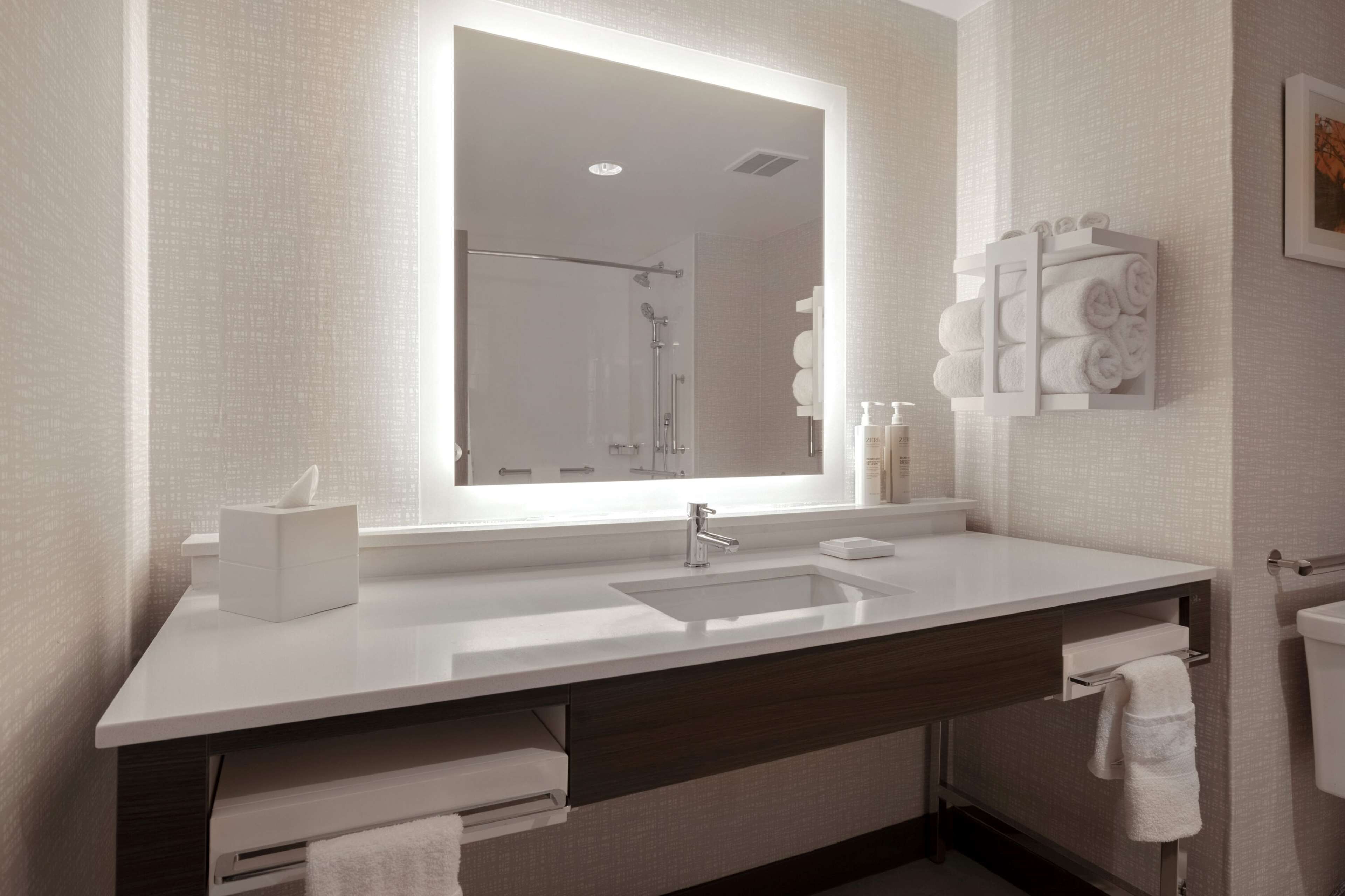 A modern bathroom with a large mirror, white sink, and towel rack.