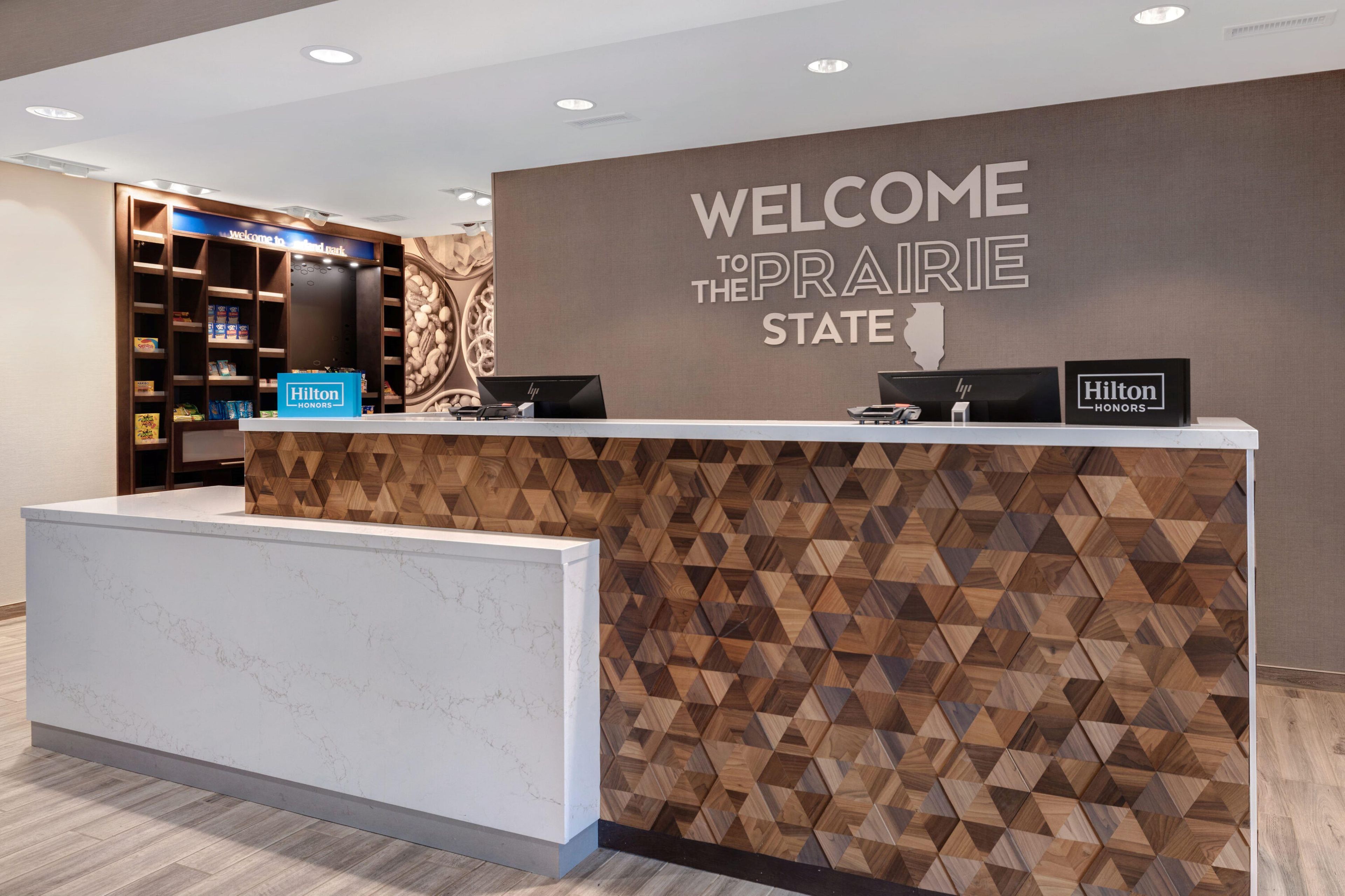 A hotel reception desk with a 'Welcome to the Prairie State' sign, a 'Hilton Honors' sign, and a 'Hilton Honors' plaque.