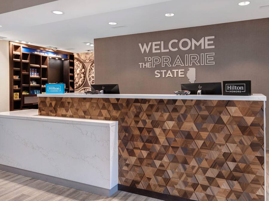 A hotel reception desk with a 'Welcome to the Prairie State' sign, a 'Hilton Honors' sign, and a 'Hilton Honors' plaque.