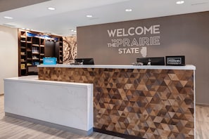 Una recepción de hotel con un cartel que dice 'Welcome to the Prairie State', un letrero de 'Hilton Honors' y una placa de 'Hilton Honors'.
