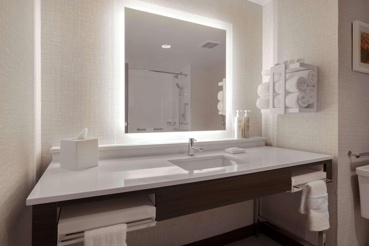 Un baño moderno con un espejo grande, lavamanos blanco y toallero.