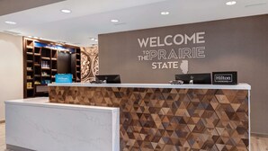 Un mostrador de recepción con un letrero que dice 'Welcome to the Prairie State', una placa de 'Hilton Honors' y un letrero de 'Hilton'.