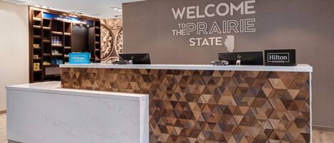 A reception desk with a 'Welcome to the Prairie State' sign, a 'Hilton Honors' plaque, and a 'Hilton' sign.