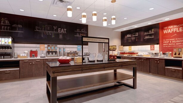 Interior moderno de una cafetería con una mesa central, barra y exhibición de menú.