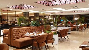 Restaurante moderno com área de estar central, apresentando um sofá e cadeiras marrons, rodeado por mesas com louças elegantemente dispostas.