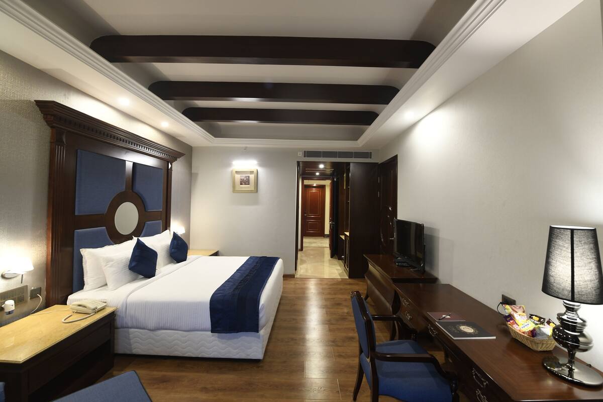 A hotel room with a bed, desk, chair, lamp, and television.