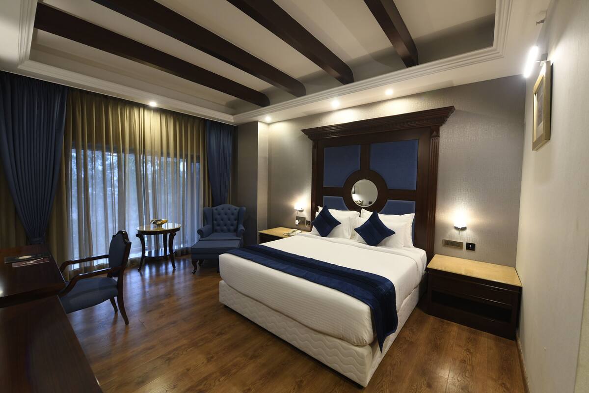 A hotel room with a large bed, a desk, a chair, and a round table.