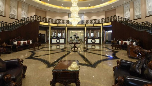 Um hall imponente com um lustre central, mobiliário trabalhado e uma escadaria majestosa.