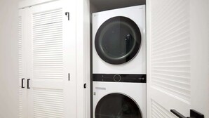 Une buanderie avec deux machines à laver superposées et une porte blanche dotée d’une poignée.