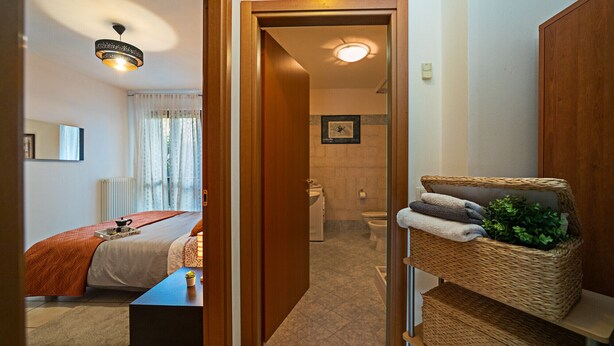 A hotel room with a bed, a small table with a plant, a wicker shelf with towels, and a bathroom visible through an open door. - Regarda - "Costa del Sole" with swimming pool and terrace (Lazise)