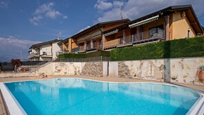 A swimming pool with a stone wall and a building with balconies in the background. - Regarda - "Costa del Sole" with swimming pool and terrace (Lazise)