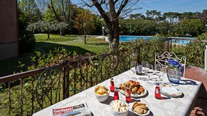 Ein Tisch im Freien, gedeckt mit Speisen, Wein und Gläsern, mit Blick auf einen Pool und Grünflächen.