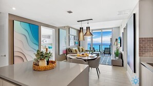A modern kitchen with a central island, dining area with a view, and a living space with a sofa and table. - Luxury Condo| Ocean View| Complementary Parking (Hollywood)