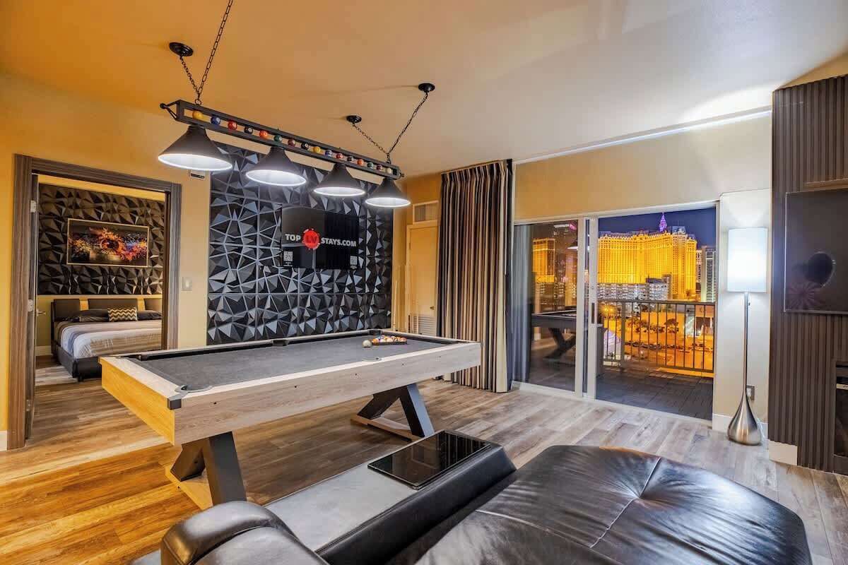 A modern room with a pool table, a sofa, and a view of a cityscape through a glass door.
