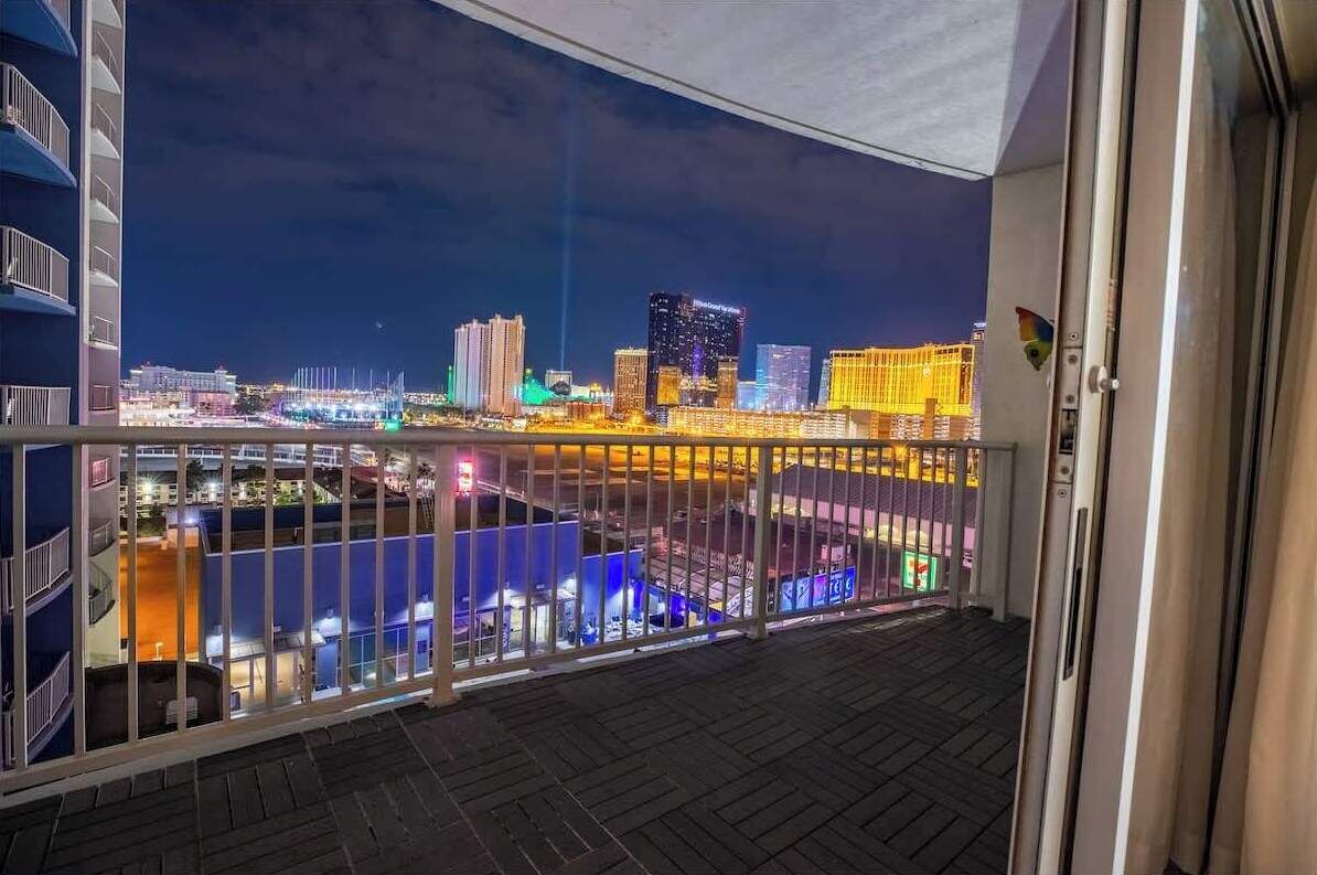 Ein Balkon mit Blick auf eine beleuchtete Stadtlandschaft bei Nacht, inklusive Gebäude und einer Uferpromenade.