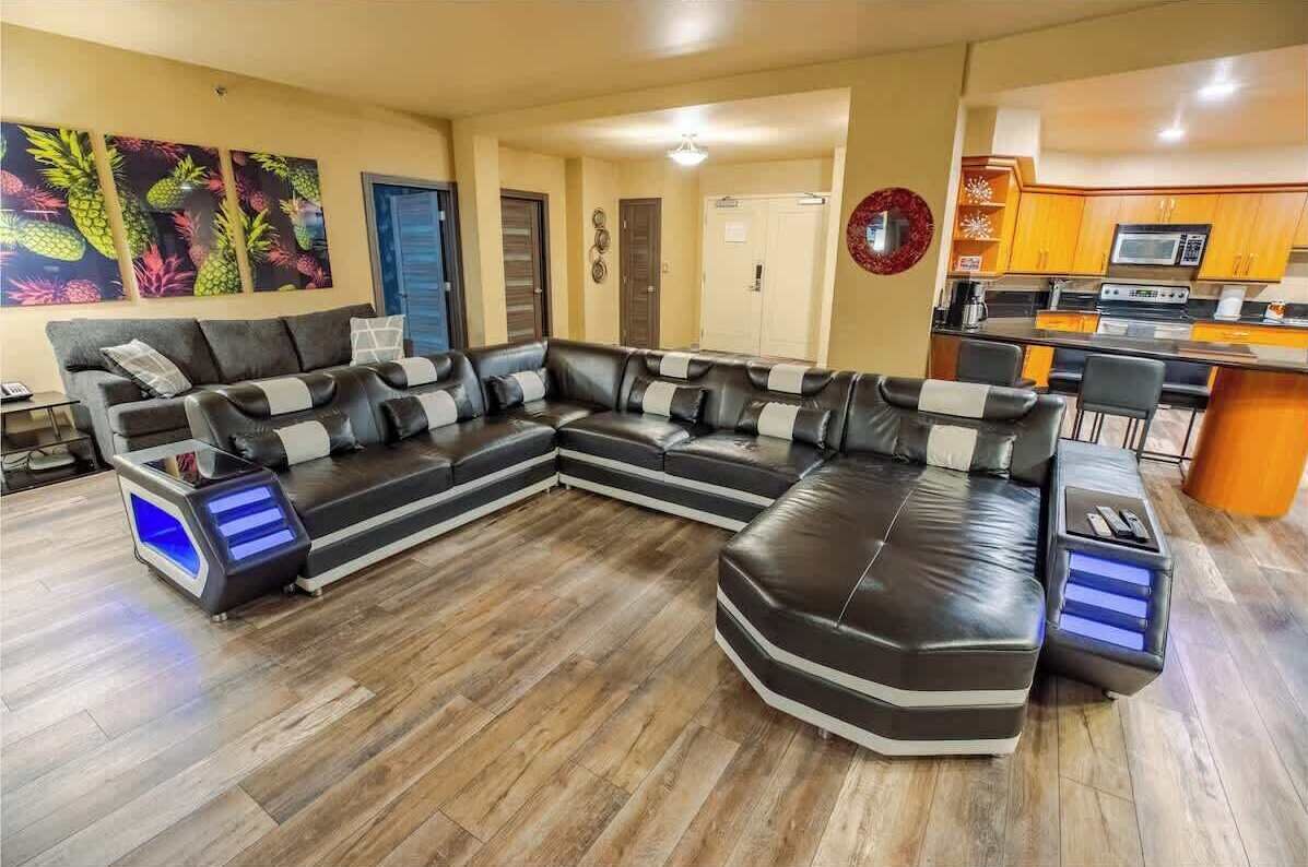 Una sala moderna con un sofá modular, una pequeña cocina y piso de madera.
