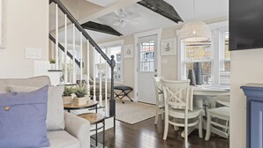 A spacious living room with a staircase, a dining area with white chairs, and a ceiling fan. - Downtown Luxury Villa on the Plymouth Waterfront (Plymouth)