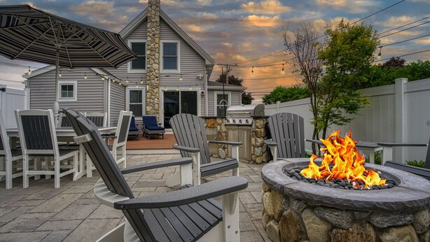 A patio area with Adirondack chairs, a stone fire pit, and a grill. - Downtown Luxury Villa on the Plymouth Waterfront (Plymouth)