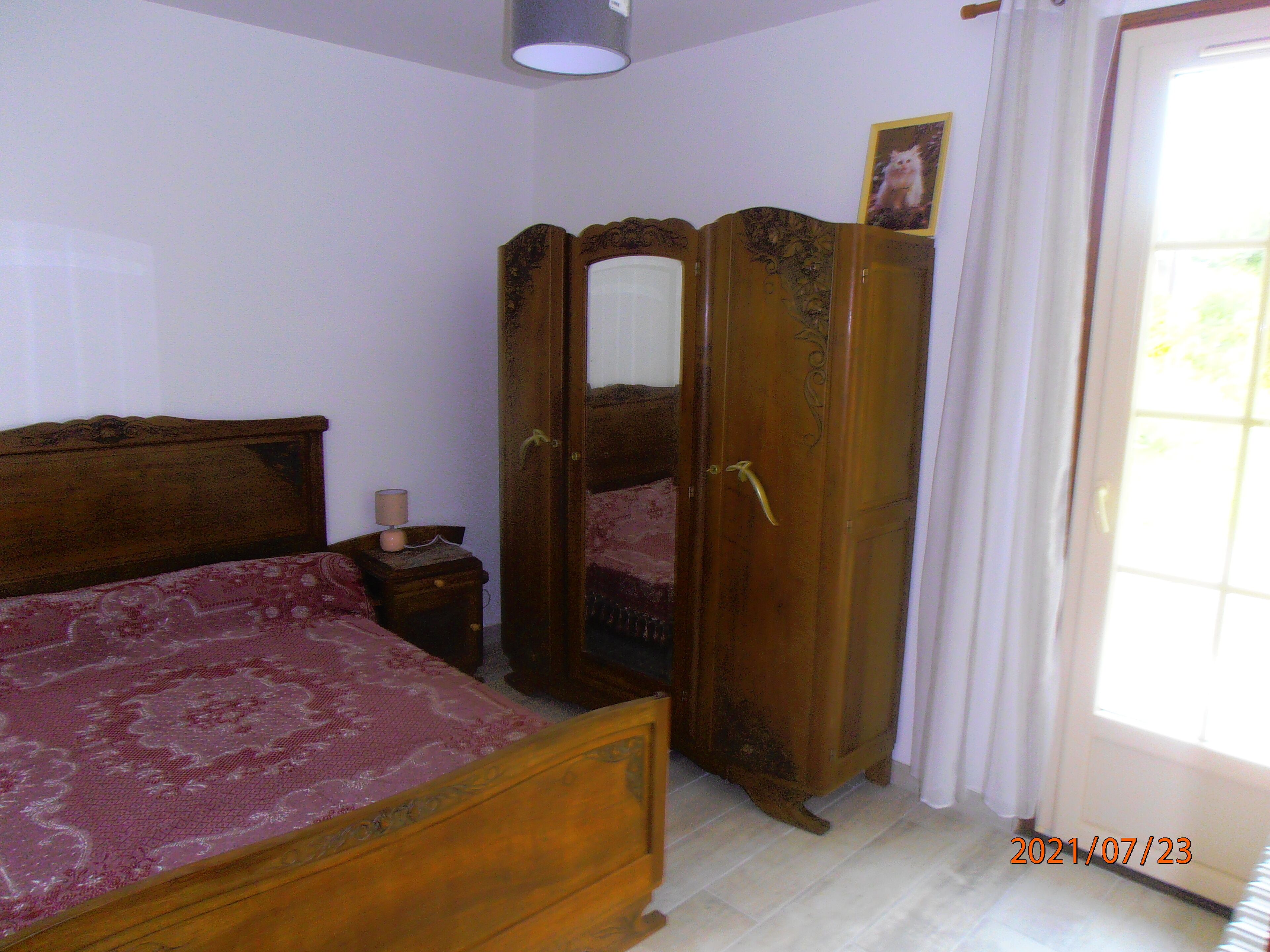 Une chambre à coucher avec un lit en bois, une table de chevet avec une lampe, une armoire et une fenêtre avec des rideaux.