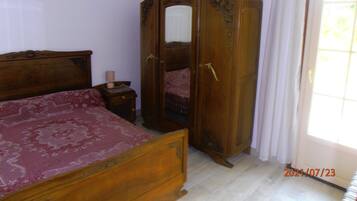 Une chambre à coucher avec un lit en bois, une table de chevet avec une lampe, une armoire et une fenêtre avec des rideaux.