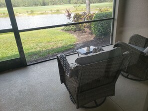 Relax in a serene space with a golf course view, featuring a wicker chair and small table.