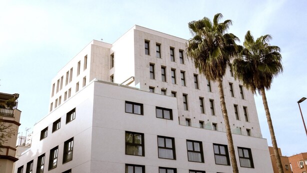 A multi-story building with a flat facade, numerous windows, and a palm tree in the foreground.