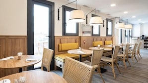 A restaurant with round tables, wicker chairs, and a wooden bench with yellow cushions.
