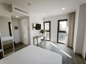 A modern hotel room with a bed, a desk, a TV, and large windows. - Petit Palace Vargas (Seville)