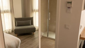 A room with a sofa, a glass shower enclosure, and a thermostat on the wall.