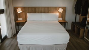 A hotel room with a large bed, wooden headboard, bedside lamps, a mirror, and a coat rack.