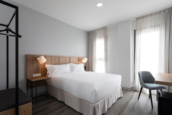 A modern hotel room with a large bed, bedside lamps, a wooden headboard, a desk, and a chair. - Petit Palace Vargas (Seville)
