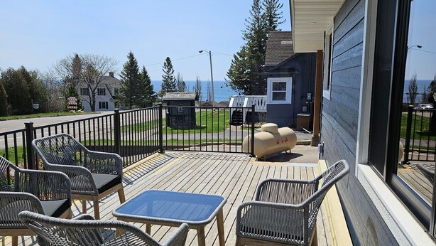 A wooden deck with outdoor furniture, a clear view of the ocean, and a building with large windows.