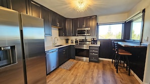 A modern kitchen with dark cabinetry, stainless steel appliances, and a central island with stools.