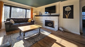 A living room with a fireplace, a sofa, a coffee table, and a TV mounted above the fireplace.