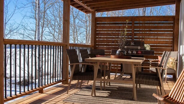 Un patio cubierto con una mesa y sillas de madera, una parrilla y vistas a árboles.