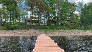 Un muelle de madera se adentra en el agua, rodeado de árboles y un edificio al fondo.