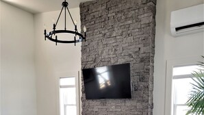 Una sala de estar moderna con chimenea de piedra, un televisor de pantalla plana montado en la pared, un sofá, dos sillones, una mesa de centro y una mesita auxiliar.