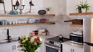 Cocina moderna con armarios blancos, encimera de madera, refrigerador de acero inoxidable, horno integrado y microondas. Hay un florero con flores sobre la encimera, y una lámpara colgante arriba.