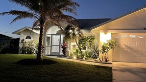 Een woonhuis met een verzorgd gazon, een palmboom en een garage.