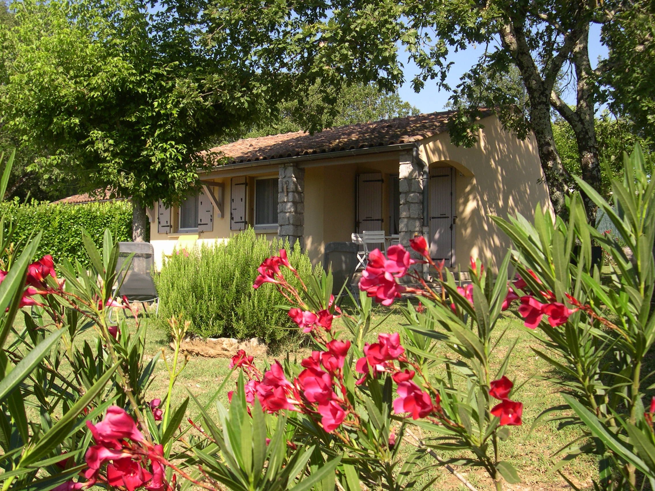 A house with a tiled roof, a stone pillar, and a garden with red flowers.