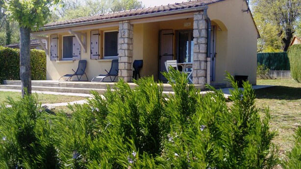 A two-story building with a stone facade, a covered porch with two lounge chairs, and a small outdoor seating area. - Charming air-conditioned gîte, Chauzon Ardèche méridionale (Chauzon)