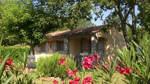 A house with a tiled roof, a stone pillar, and a garden with red flowers. - Charming air-conditioned gîte, Chauzon Ardèche méridionale (Chauzon)