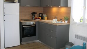 A compact kitchen with a microwave, oven, sink, and a small countertop area with a bowl of fruit and a coffee maker. - Charming air-conditioned gîte, Chauzon Ardèche méridionale (Chauzon)